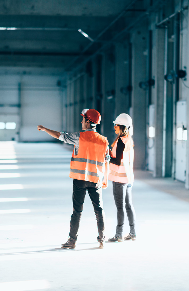 Two technicians in safety vests and hard hats in an industrial hall